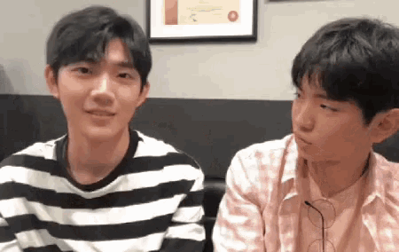 two young men are sitting next to each other and looking at each other . one of the men is wearing a striped shirt .