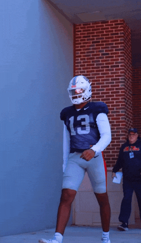 a football player with the number 13 on his jersey stands in front of a brick wall
