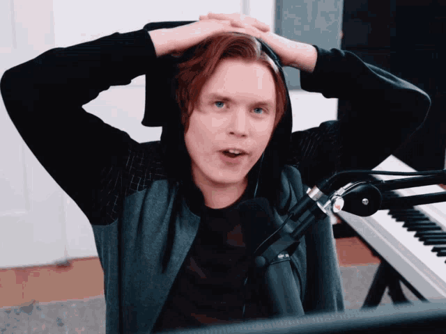 a man wearing a hoodie is sitting in front of a microphone with his hands on his head