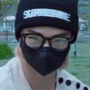 a person wearing a mask and glasses is wearing a black beanie .