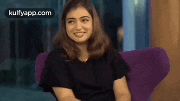a woman is sitting in a purple chair smiling .