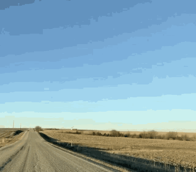 a dirt road going through a field with a blue sky behind it