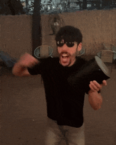 a man wearing sunglasses and a black shirt is holding a black object that looks like a flamethrower