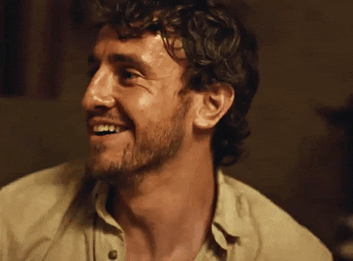 a man with a beard and curly hair is smiling and looking at the camera .