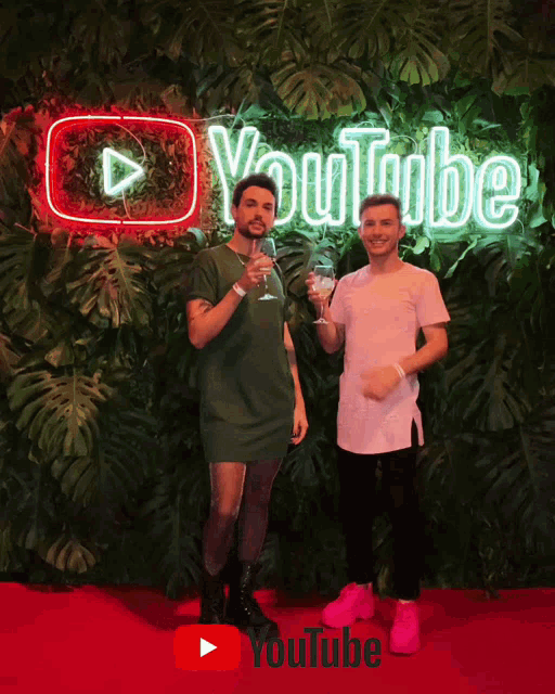 two men stand in front of a youtube neon sign