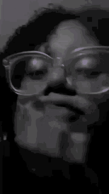 a black and white photo of a woman wearing glasses covering her mouth .