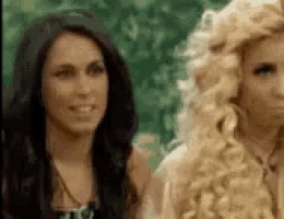 two women are standing next to each other and one of them is wearing a blonde wig .