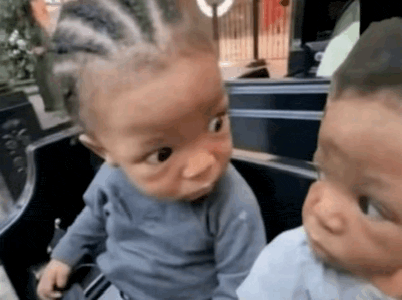 two babies are looking at each other while sitting next to each other .