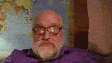 a man with glasses and a beard looks at the camera in front of a world map