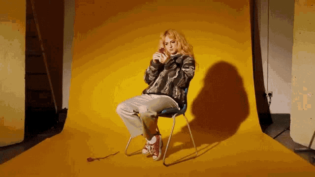 a woman sits in a chair with a yellow background