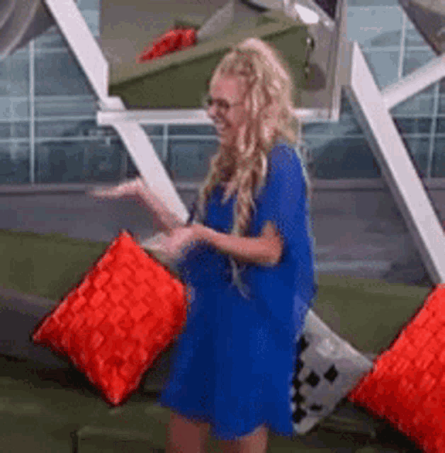 a woman in a blue dress is standing in front of a green couch surrounded by red pillows .