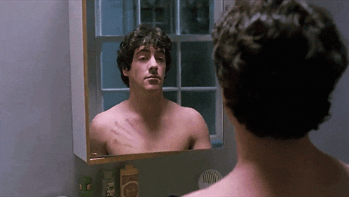 a man without a shirt is looking at himself in the mirror