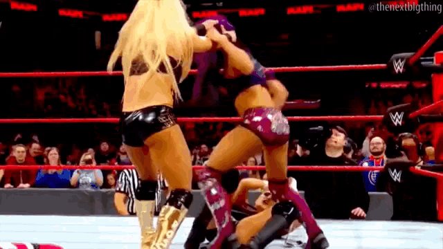 two women are wrestling in a wrestling ring with a referee in the background .
