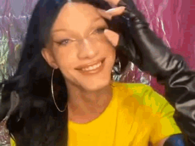 a woman wearing a yellow shirt and black gloves is smiling while another person holds her eye .