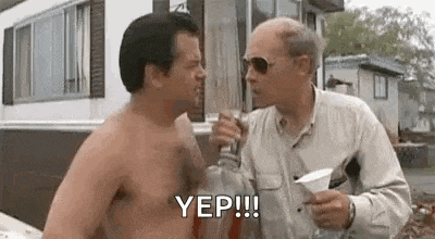 a shirtless man is standing next to another shirtless man holding a bottle of liquor .
