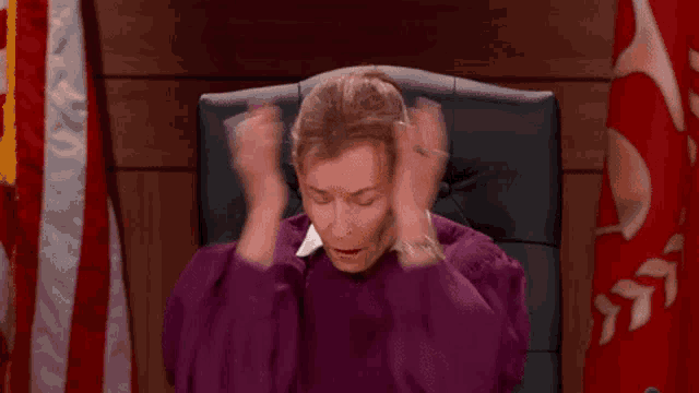 a woman in a purple robe is sitting in a chair holding her hands to her head .