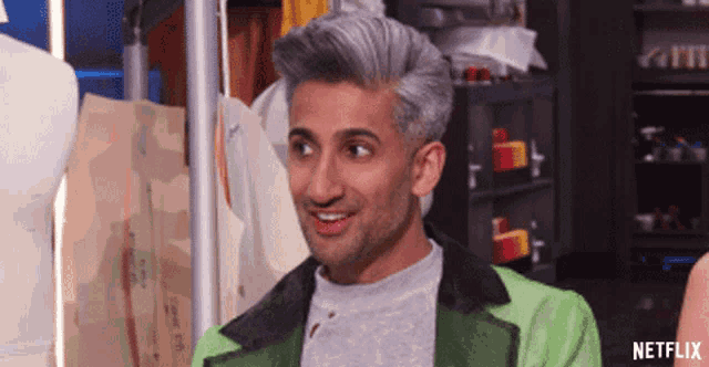 a man with gray hair is wearing a green jacket and a gray shirt .