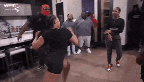 a group of people are dancing in a room with a woman in the middle .