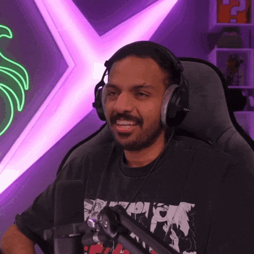 a man wearing headphones sits in front of a microphone and a neon sign that says ' r ' on it