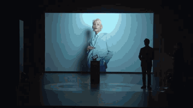 a man in a suit stands in front of a large screen
