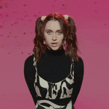 a woman wearing a black turtleneck and a black and white dress stands in front of a pink background with confetti