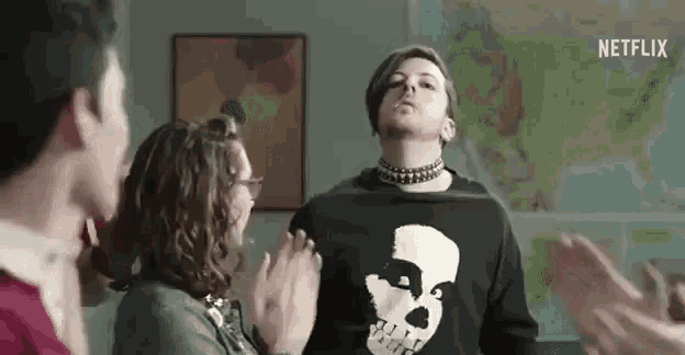 a man wearing a sweater with a skull on it is standing in a room with other people .