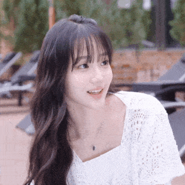 a young woman wearing a white top and necklace smiles
