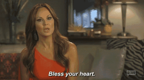 a woman in an orange dress is sitting on a couch and says bless your heart .