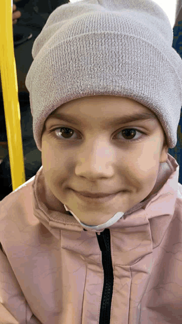 a little girl wearing a pink jacket and a white beanie