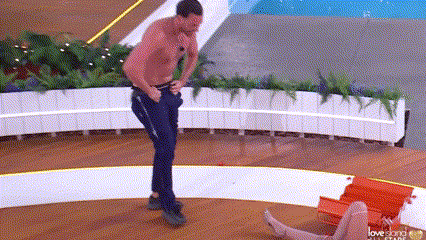 a man without a shirt is standing next to a woman laying on a beach chair .