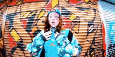 a woman is standing in front of a graffiti wall wearing a blue jacket and a hat .