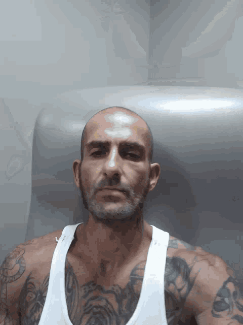 a man with a beard and a white tank top has a tattoo on his chest