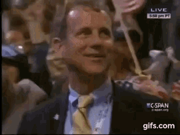 a man in a suit and tie is smiling in front of a crowd on a live tv channel