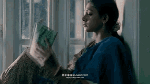 a woman is sitting in front of a window reading a book