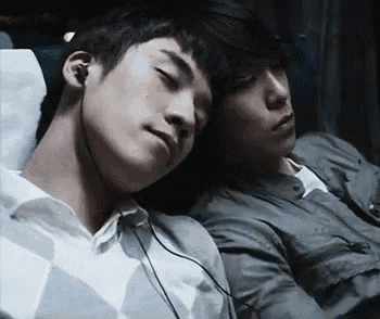 two young men are sleeping next to each other on a bus while listening to music .