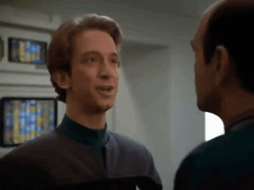 two men are standing next to each other in a room and one of them is smiling .