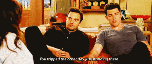 two men are sitting on a couch talking to a woman and one of them says you tripped the other day just standing there .