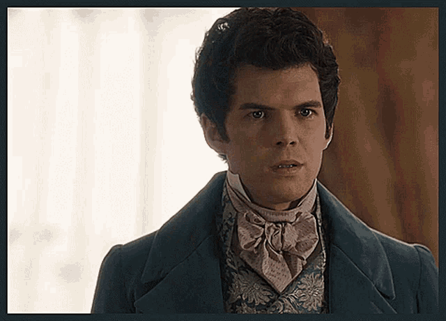 a man wearing a blue coat and a pink tie looks at the camera