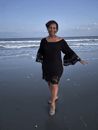 a woman in a black lace dress stands on the beach