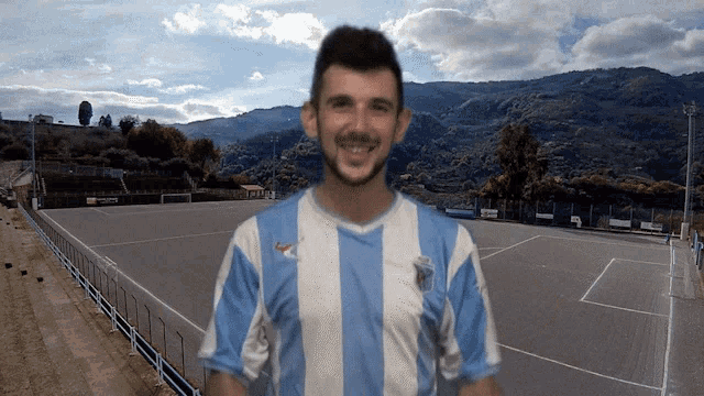 a man wearing a blue and white striped shirt with a soccer field in the background
