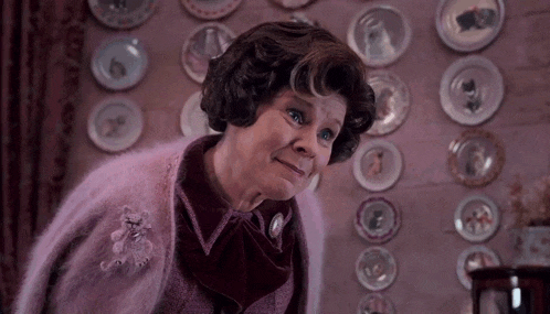 a woman in a pink sweater is standing in front of a wall with plates on it