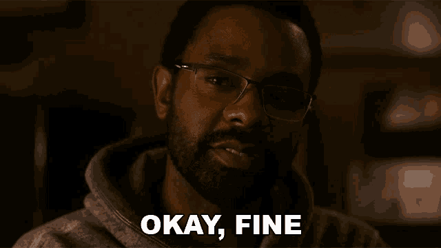 a man with glasses says " okay fine " in a dark room