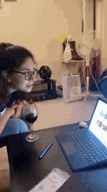 a woman is sitting at a table drinking wine and looking at a laptop .