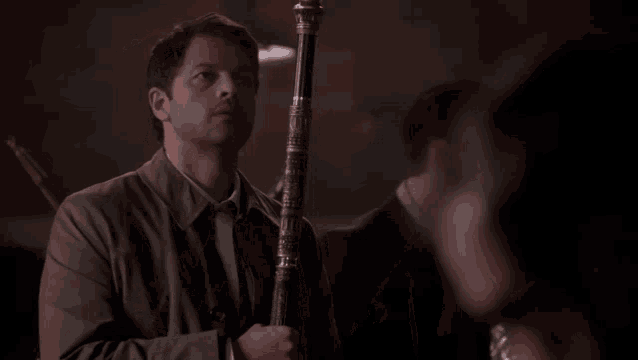 a man in a trench coat is holding a stick in his hand