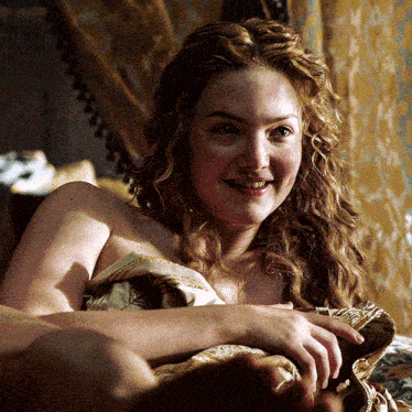 a naked woman with curly hair is smiling and laying on a bed