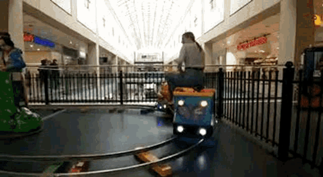 a woman is riding a toy train in a mall .