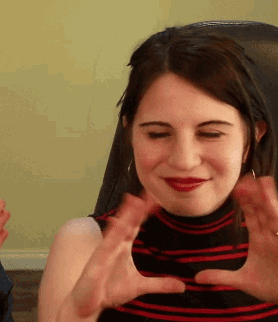 a woman in a black and red striped shirt is making a heart with her hands