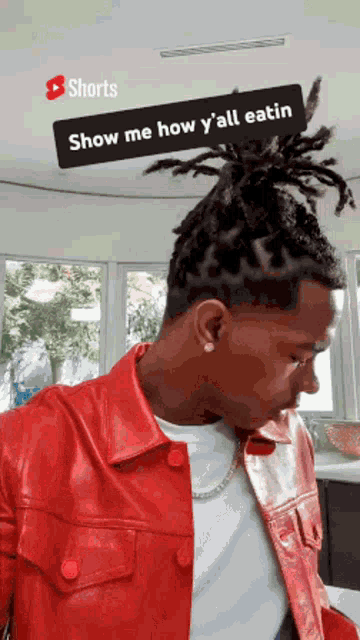 a man is wearing a red leather jacket and a white shirt and has dreadlocks in his hair .