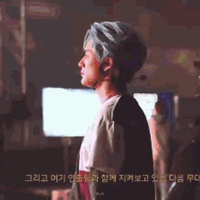 a man with green hair is standing in front of a screen with foreign writing on it