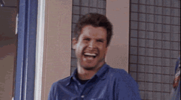a man in a blue shirt is laughing while standing in front of a window .